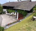 A well-maintained garden area with a patio, outdoor furniture, and a house with a tiled roof and greenery.