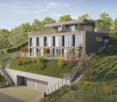 Modern two-story house with a flat roof, large windows, and a balcony on the upper level. The house is situated on a hillside with a landscaped garden and a covered garage at the base.