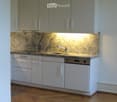 Modern kitchen with white cabinets, granite countertop, and wooden flooring.