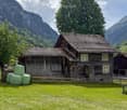 Wooden alpine house, stone chimney, wooden fence, green hay bales, mountains, grass field