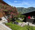 Garden with a well-maintained lawn, flowering shrubs, a stone pathway, and a view of the surrounding mountains.