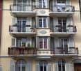 4 story building, beige paint, white shutters, balconies, windows, metal railings, potted plants