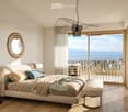 Modern bedroom with a large bed, nightstands, a round mirror, and a balcony overlooking the sea.