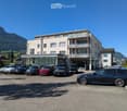 3 story building with many windows, balcony, outdoor parking lot, surrounded by mountains