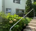 white painted house, raised ground floor, stairs leading to entrance, garden with shrubs and flowers