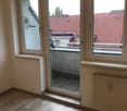 Empty room with wooden flooring, white walls, large windows, radiator, and a view of rooftops through the open window.