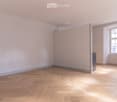 Empty room with light-colored walls, wooden floor, and a single window letting in natural light.