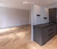 Modern kitchen with dark grey cabinets, a black countertop, and a double sink. The floor is made of light wooden parquet, and the walls are painted in a light grey color. The kitchen features built-in storage and a sleek, contemporary design.