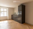 Modern kitchen with grey cabinets, a sink, a faucet, and an oven, featuring wooden flooring and a large window.