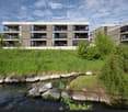 Modern apartment building with multiple floors, balconies, and a grassy area in front