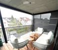 balcony with wooden floor, black railing, white wicker chairs, wooden coffee table, white cushions, black screen