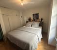 A well-lit bedroom with a double bed, pillows, a headboard, a wall-mounted light fixture, a cabinet, and a picture frame on the wall.