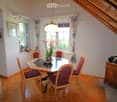 Dining room with wooden floor, round wooden dining table, six chairs, flower pot, cabinet, and picture frame on the wall.