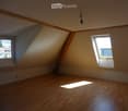 Empty attic room with wooden floors, slanted ceilings, and two windows allowing natural light to enter.