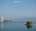 A scenic view of a lake with a fountain spraying water into the air, surrounded by trees and distant hills.
