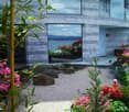 Modern house with large glass windows overlooking a scenic water view, surrounded by a well-maintained garden with colorful flowers and rocks.