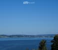 A scenic view of a large lake surrounded by green hills and a town in the distance, with a clear blue sky overhead.