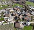 Aerial view of a residential area with multiple houses, apartment buildings, and green spaces. Some buildings have solar panels on their roofs, and there are construction cranes visible in the area.