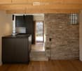 modern kitchen with black cabinets, wooden floor, stone wall, open door leading to outdoor area