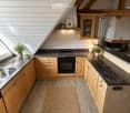 Modern kitchen with wooden cabinets, granite countertops, a central island, and a cozy rug. Features include a stove, sink, and decorative potted plants.