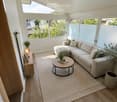 Bright living room with wooden flooring, large windows, a sectional sofa, coffee table, side table, and potted plants.