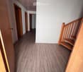 Empty hallway with wooden flooring, white walls, and several open doors leading to other rooms. A wooden staircase is visible on the right side.
