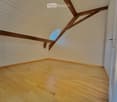 Empty attic room with wooden floor, white walls, and exposed wooden beams on the ceiling. Features a skylight window and a door.