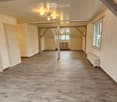 large room, wooden flooring, white walls, multiple doors, windows, radiators, central lighting