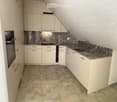 Modern kitchen with white cabinets, granite countertop, sink, and built-in oven. Light-colored tiled floor.