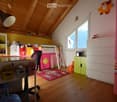 Bright, colorful children's bedroom with wooden floors, slanted wooden ceiling, bunk bed, desk, bookshelf, and colorful storage bins.