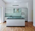 Modern kitchen with white cabinets, a central island, and a glass countertop. Features include a built-in oven, a range hood, and a sink.