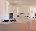 Modern kitchen with white cabinets, a central island, and stainless steel appliances including an oven and sink. The countertop features a few small items like a bowl and a bottle.