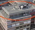 A multi-story building with a flat roof, visible air conditioning units, and surrounding structures.