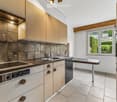 Modern kitchen with light wooden cabinets, stainless steel appliances, and a central island table.