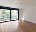 Empty room with light wooden flooring, white walls, and large sliding glass doors leading to a balcony or outdoor area.