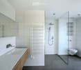 Modern bathroom with a large sink, toilet, shower, radiator, and mirror. The space features white tiles and a sleek design.
