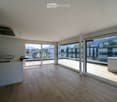 Bright, open-plan room with wooden flooring, large glass sliding doors leading to a balcony, and a scenic mountain view.