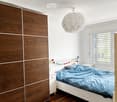 Modern bedroom with a white bed, blue bedding, a wooden wardrobe, and a round pendant light.