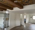 An unfurnished room with wooden flooring, white walls, and a decorative cabinet. The room features a large window, a door leading to another space, and a modern spherical lamp on a stand.