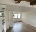 Empty room with wooden flooring, white walls, and a window with white frame. Exposed wooden beams on the ceiling.