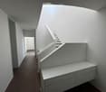 Modern hallway with white walls, wooden flooring, and a staircase leading upwards. The hallway features built-in storage units and a neutral color palette.