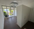 Empty room with wooden flooring, large glass sliding doors leading to a balcony with a scenic view, white built-in wardrobes, and a modern ceiling light fixture.
