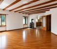 Empty room with wooden flooring, white walls, large windows, and a visible fireplace in the background.