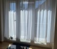 Empty room with large sliding glass door and white curtains, wooden floor, and a small rug near the door.