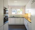 Modern kitchen with white cabinets, stainless steel oven, sink, and a window overlooking a balcony.