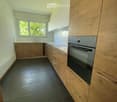 Modern kitchen with light wooden cabinets, stainless steel oven, dark tiled floor, and white countertops.