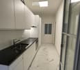 Modern kitchen with white cabinets, black countertop, stainless steel sink, and marble flooring.