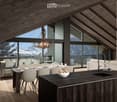 Modern, open-concept living and dining area with exposed wooden beams, large windows offering a mountain view, a dining table with chairs, a kitchen island, a sofa, a fireplace, and a chandelier.