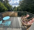 Balcony with a turquoise table, two turquoise chairs, and two wooden deck chairs with patterned cushions, surrounded by a metal railing and bamboo screen.