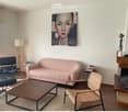 Modern living room with a pink sofa, wooden coffee table, black leather chair, wicker chair, floor lamp, fireplace, and artwork on the wall.